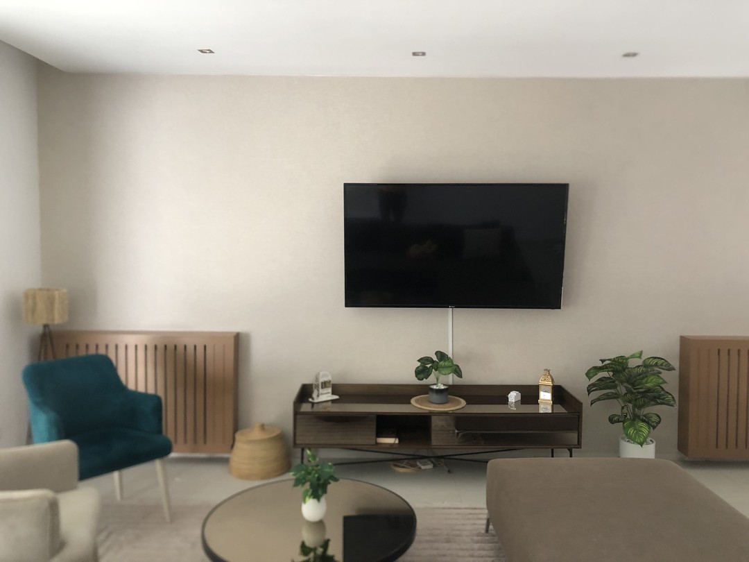 Salon minimaliste — murs beige texturés, fauteuil bleu canard et TV murale